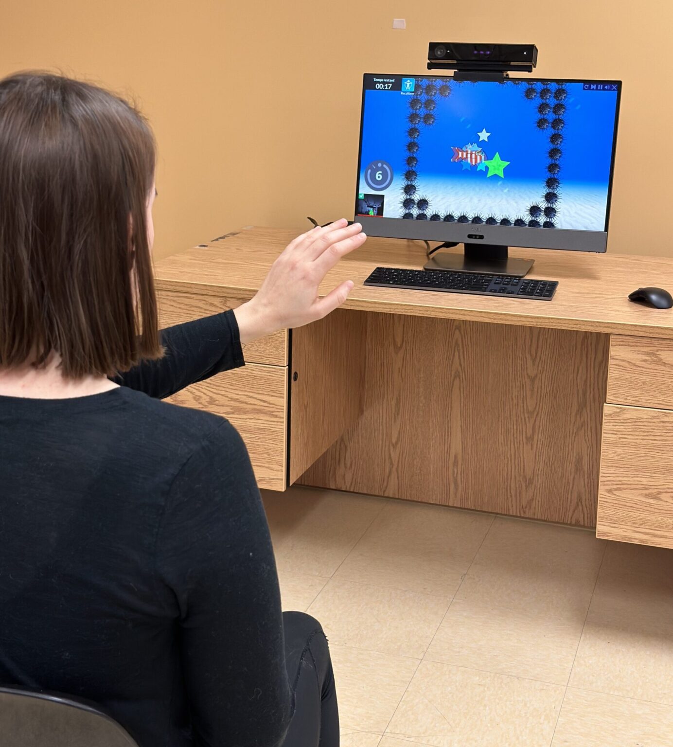 Personne interagissant avec un jeu sérieux sur écran à l’aide de gestes pour un entraînement en réadaptation.