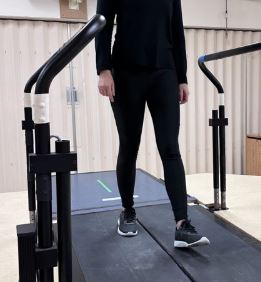 Personne effectuant un entraînement de la marche sur un tapis roulant à double courroie avec rampes de soutien.